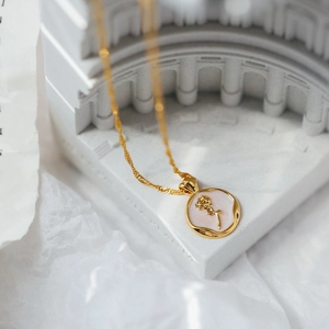 Collier vintage avec pendentif rose dorée et nacre sur support architectural blanc élégant
