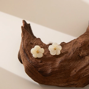 Detail of flower stud earrings featuring white shell petals and gold center on wood