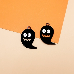 Macro shot of two black Halloween ghost charms with cute faces on orange-beige background.