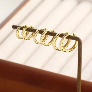 Detailed view of three pairs of golden hammered hoop earrings on a metal display stand