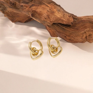 Minimalistische Gold-Creolen mit poliertem 18k Herzanhänger vor einem natürlichen Hintergrund