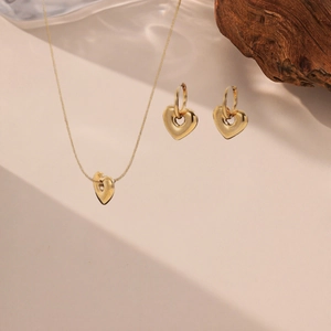 Detailansicht von goldenem Herzanhänger-Halsketten und Ohrring-Set auf Holz-Deko