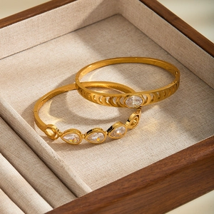 Close-up of gold stainless steel bangles with teardrop zircon inlays in a wooden box.