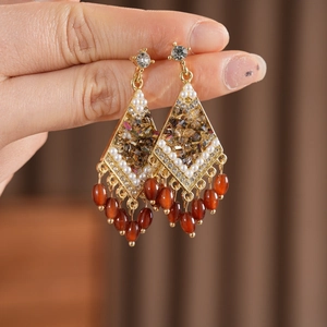 Primer plano de pendientes vintage en forma de rombo con cristales y borlas rojas