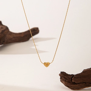 Detailed view of a golden heart pendant necklace on minimalist dark wood and beige background