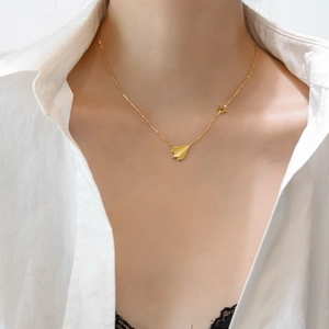 Collier avion en papier doré avec petite étoile porté sur chemisier blanc