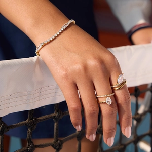 Primo piano di eleganti anelli d'oro a onda e braccialetto tennis in zircone sulla mano