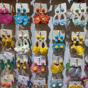 A variety of colorful handmade woven floral resort style earrings on jewelry display