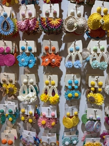 Close-up of various colorful handmade woven straw earrings with floral and pearl designs.