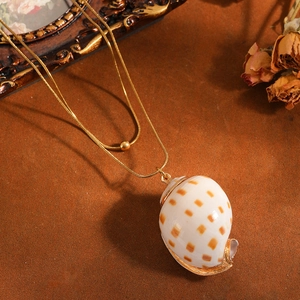 Close-up detail of a natural speckled seashell pendant on a double-layer gold chain