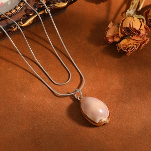 Macro view of a natural shell pendant on a double-layered stainless steel snake chain.