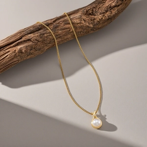 Élégant collier à pendentif perle dorée présenté sur une branche avec ombres créatives