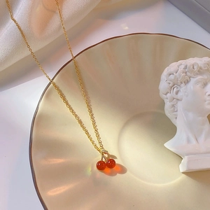 Collier élégant en chaîne dorée avec pendentif cerise rouge sur plat céramique