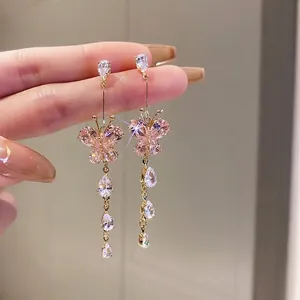 Close-up of pink butterfly earrings with dangling crystal teardrops in gold finish