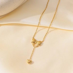 Elegante goldene Halskette mit Schleife und Herzanhänger auf Stoffhintergrund