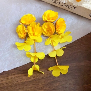 Détail en gros plan de boucles d'oreilles fleurs en résine jaune sur fond texturé.