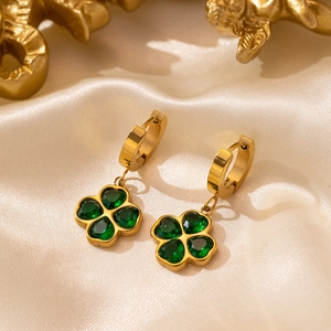 Golden clover drop earrings with emerald heart stones on ivory silk background