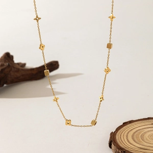 Golden clover flower necklace with square accents and star charms on wooden background