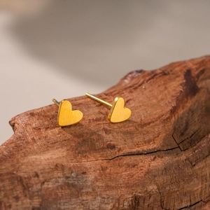 Minimalist golden heart stud earrings with brushed metal texture on a natural wood surface