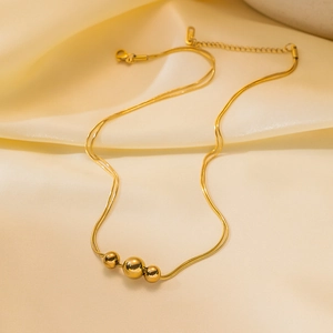 Double-layered gold snake chain necklace with three metallic beads on beige silk cloth