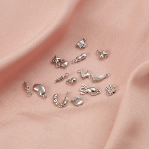 Detailed view of polished stainless steel charms in assorted shapes on pink fabric