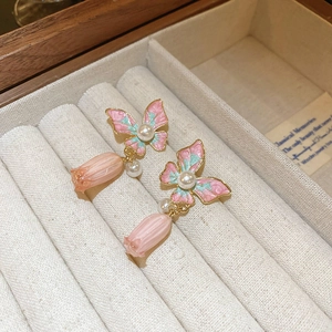 Detail van vlinderoorbellen met roze klokjesbloemen en parels in een luxe sieradendoos