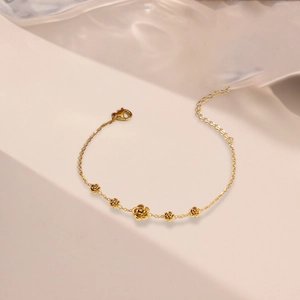 Bracelet élégant en acier titane doré avec cinq breloques camélia sur fond blanc épuré