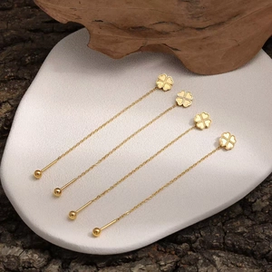 Minimalist gold clover long chain earrings displayed on a premium stone platform