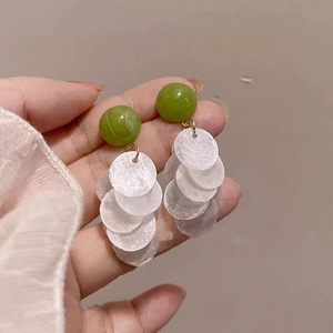 Close-up of elegant long tassel earrings with green beads and white shell discs.