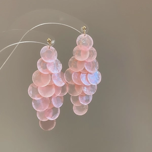 Dettaglio dei dischi di conchiglia rosa traslucidi su lunghi orecchini a nappa eleganti.