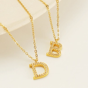 Détail du collier en acier inoxydable doré avec pendentifs lettres D et B sertis de strass