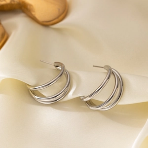 Minimalist silver triple-layered C-shaped stud earrings on soft beige silk fabric