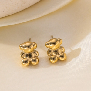 Polished golden bear-shaped earrings on beige silk fabric with minimalist luxury aesthetic