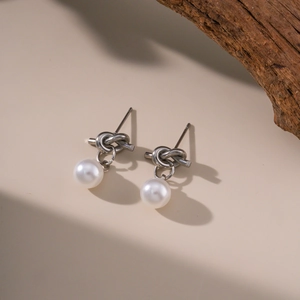 Elegant French vintage style knot stud earrings with drop pearl on a rustic wood background