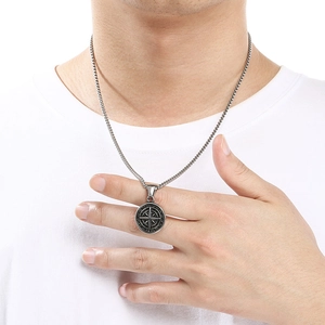 Detail of a vintage stainless steel compass pendant necklace on a man wearing a white shirt.