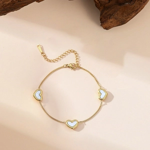 Gold stainless steel heart charm bracelet with white shell inlays on a beige background