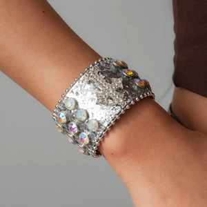 Detail of silver glitter leather cuff bracelet featuring rhinestone cross and iridescent gems.