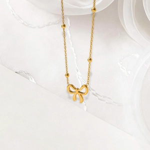 Collier élégant doré avec pendentif nœud sur fond de soie blanche soyeuse