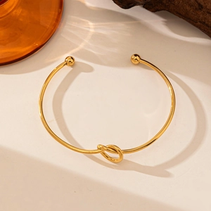 Minimalist 18K gold plated knotted open bangle with ball ends on a textured surface