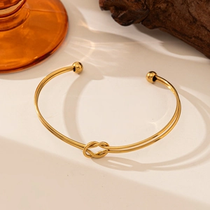 Detail view of gold knotted double-line bangle with polished finish on wooden stand