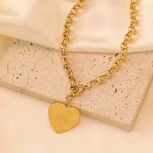 Vue détaillée d'un pendentif cœur doré avec texture rayon de soleil sur une chaîne à maillons.