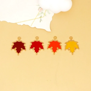Detail of four maple leaf enamel charms in autumn colors arranged on a yellow background