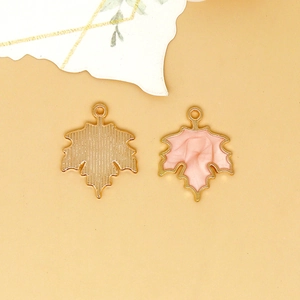 Detailed view of a pink enamel maple leaf charm with gold-tone textured metal backing.