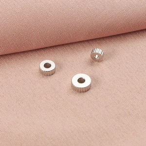 Macro view of stainless steel ribbed gear beads on a pink textured fabric background.