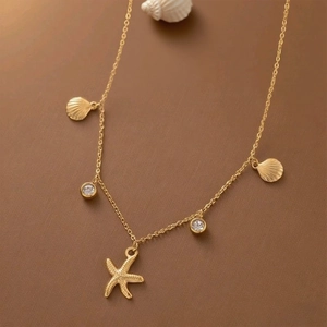 Elegant gold starfish and seashell necklace with zircon accents on a beach-themed background