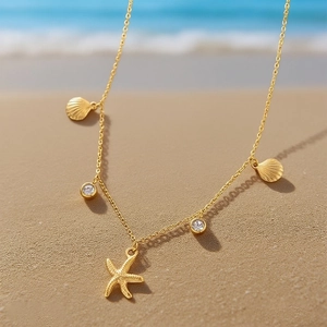 Close-up of gold starfish and shell charms on a necklace at a sunny beach setting