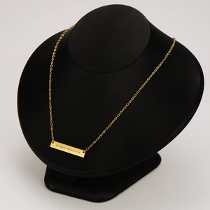 Vista detallada del collar con barra grabada en oro de 18k sobre un soporte negro.