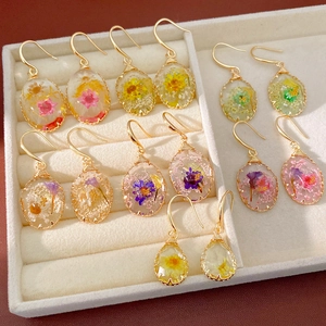 Detailed view of various oval and teardrop resin earrings with embedded real dried flowers.