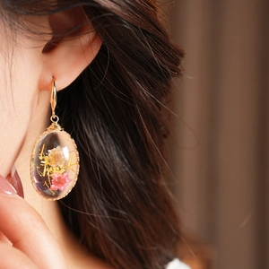 Close-up of pastoral oval resin earrings with vibrant dried flowers and gold hook