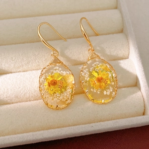 Detail view of oval resin earrings with yellow dried flowers in a beige jewelry box